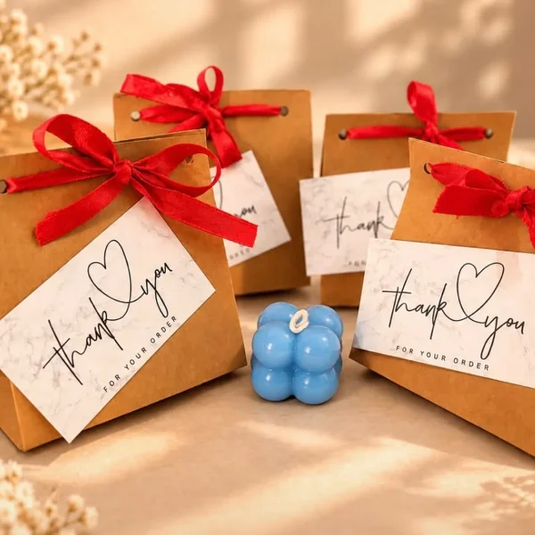 Small blue bubble cube soy candle between kraft gift bags with red ribbons